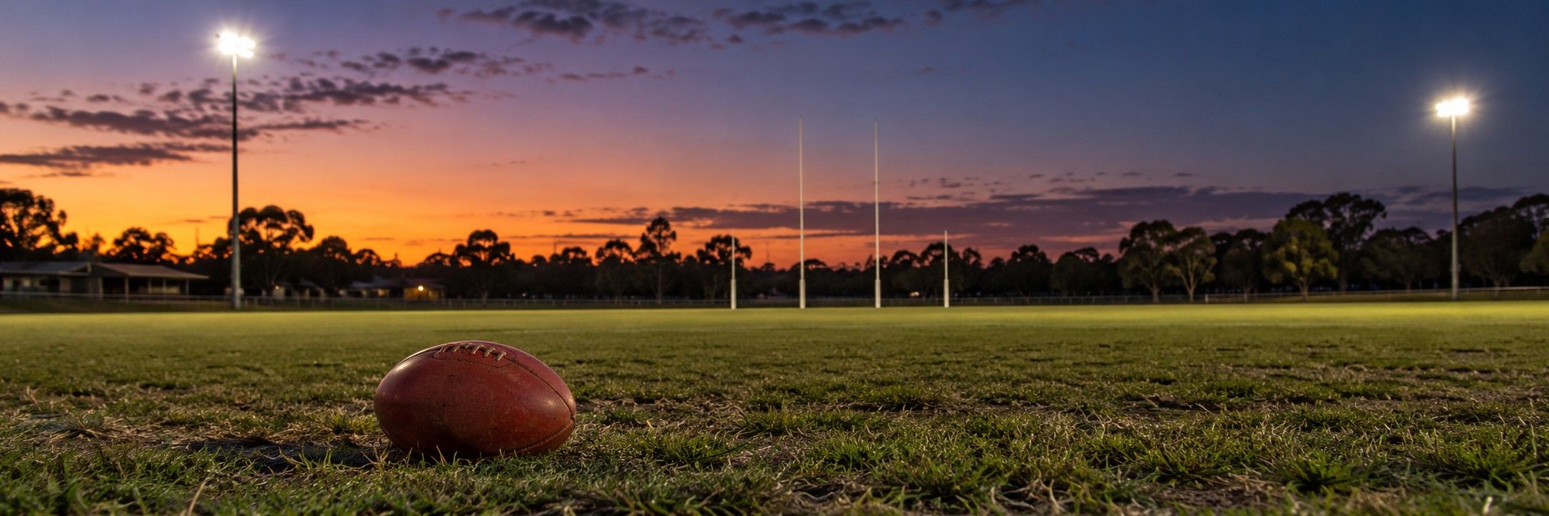 An empty football oval at dusk, a ball on the grass